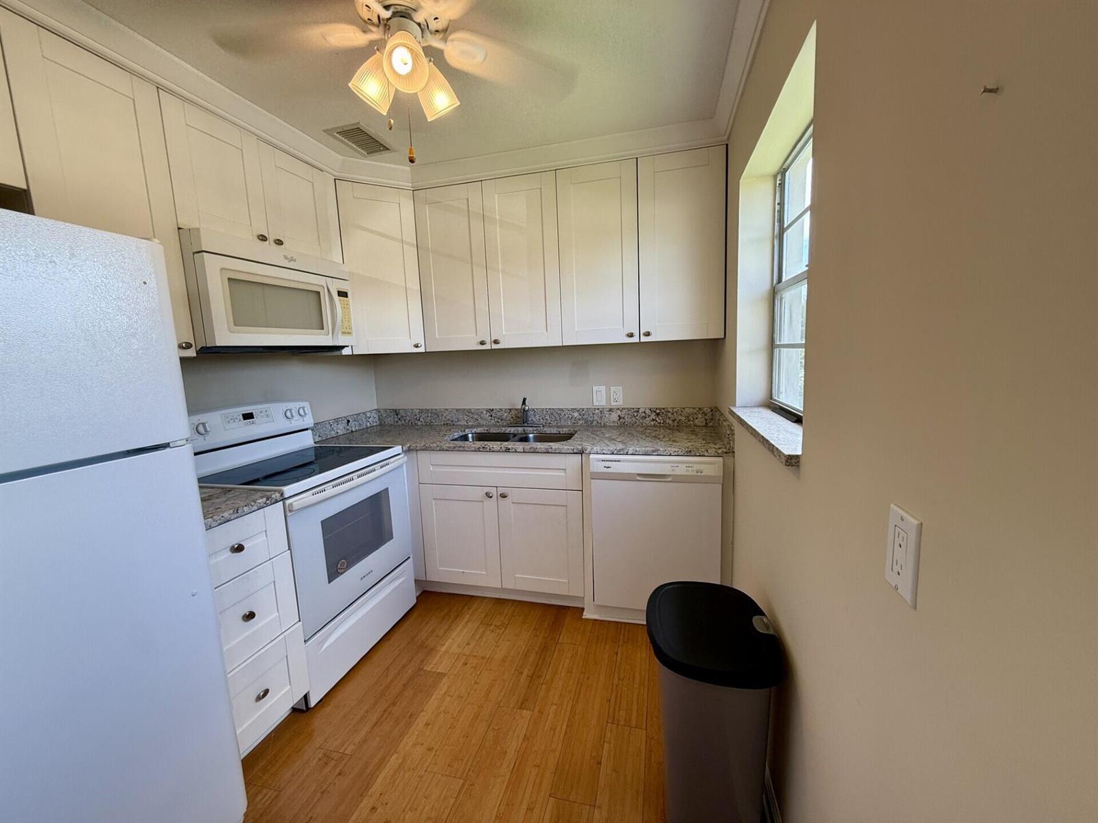 A kitchen features white cabinets, granite countertops, white appliances, and light wood flooring — 73 Hastings E, West Palm Beach FL 33417, WEST PALM BEACH, FL