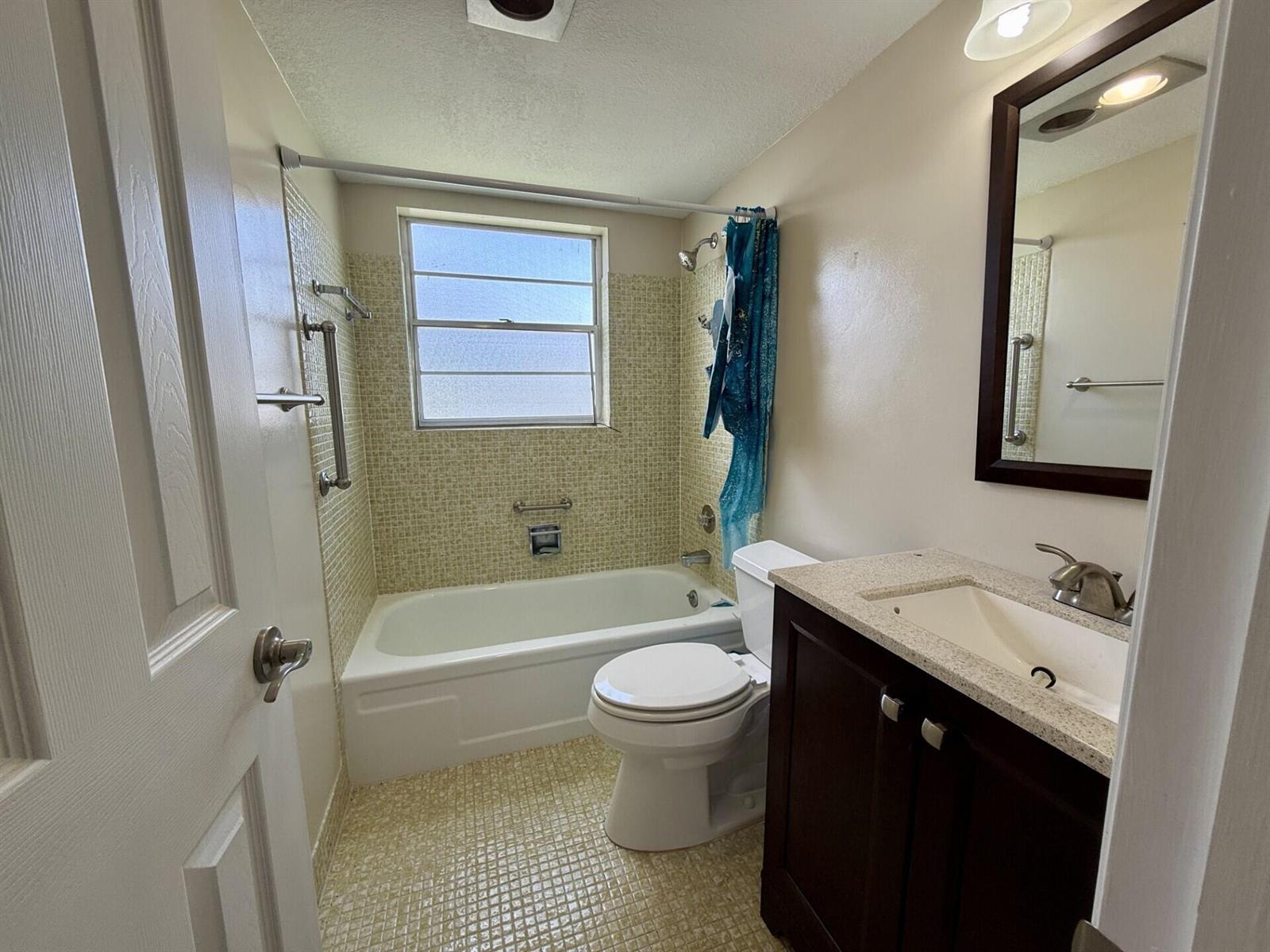 A bathroom features a tub-shower combo with yellow mosaic tile, a toilet, and a vanity — 73 Hastings E, West Palm Beach FL 33417, WEST PALM BEACH, FL