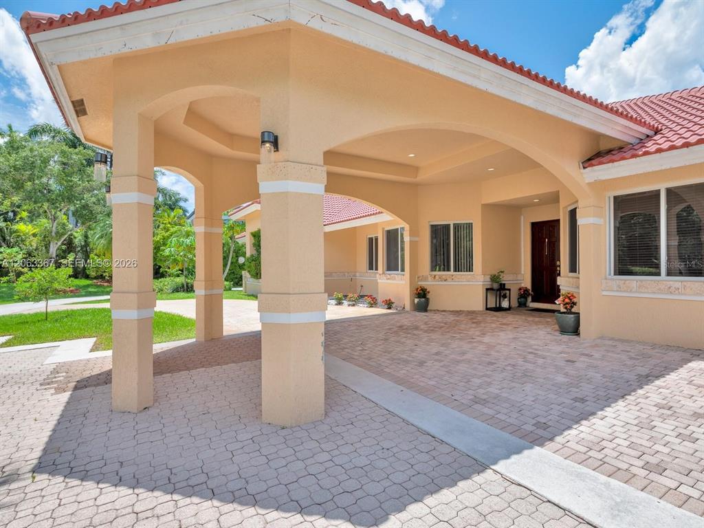A covered porte-cochère with beige stucco columns leads to the front entrance of a house — 2710 WALKERS WAY, WESTON, FL
