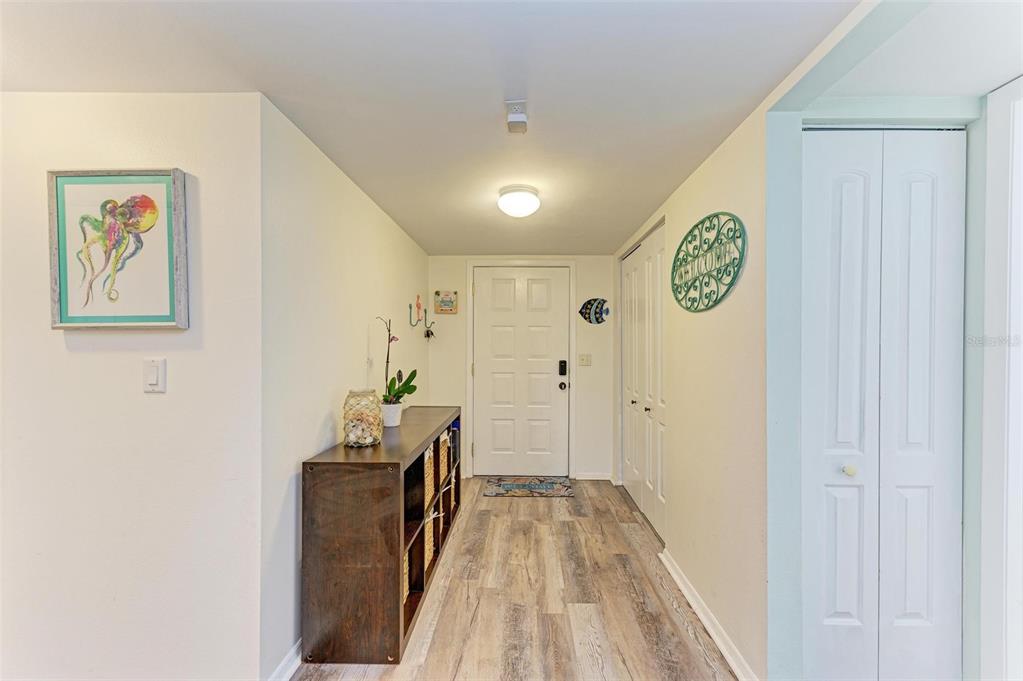 A hallway with wood-look flooring, a dark storage unit, and a white front door — 6336 7TH AVENUE W UNIT 6336, BRADENTON, FL