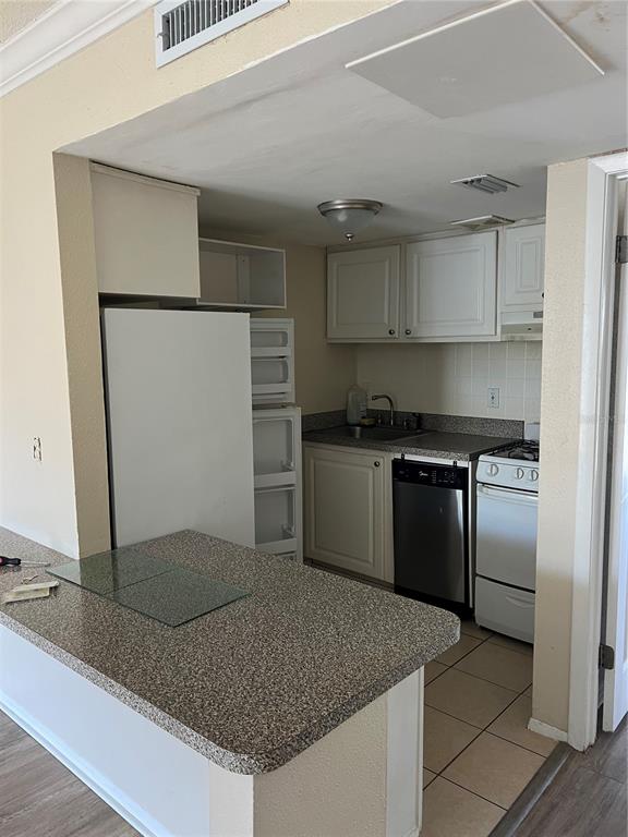 A small kitchen features white cabinets, a stainless steel dishwasher, and a speckled countertop island — 136 BLUE POINT WAY UNIT 310, ALTAMONTE SPRINGS, FL