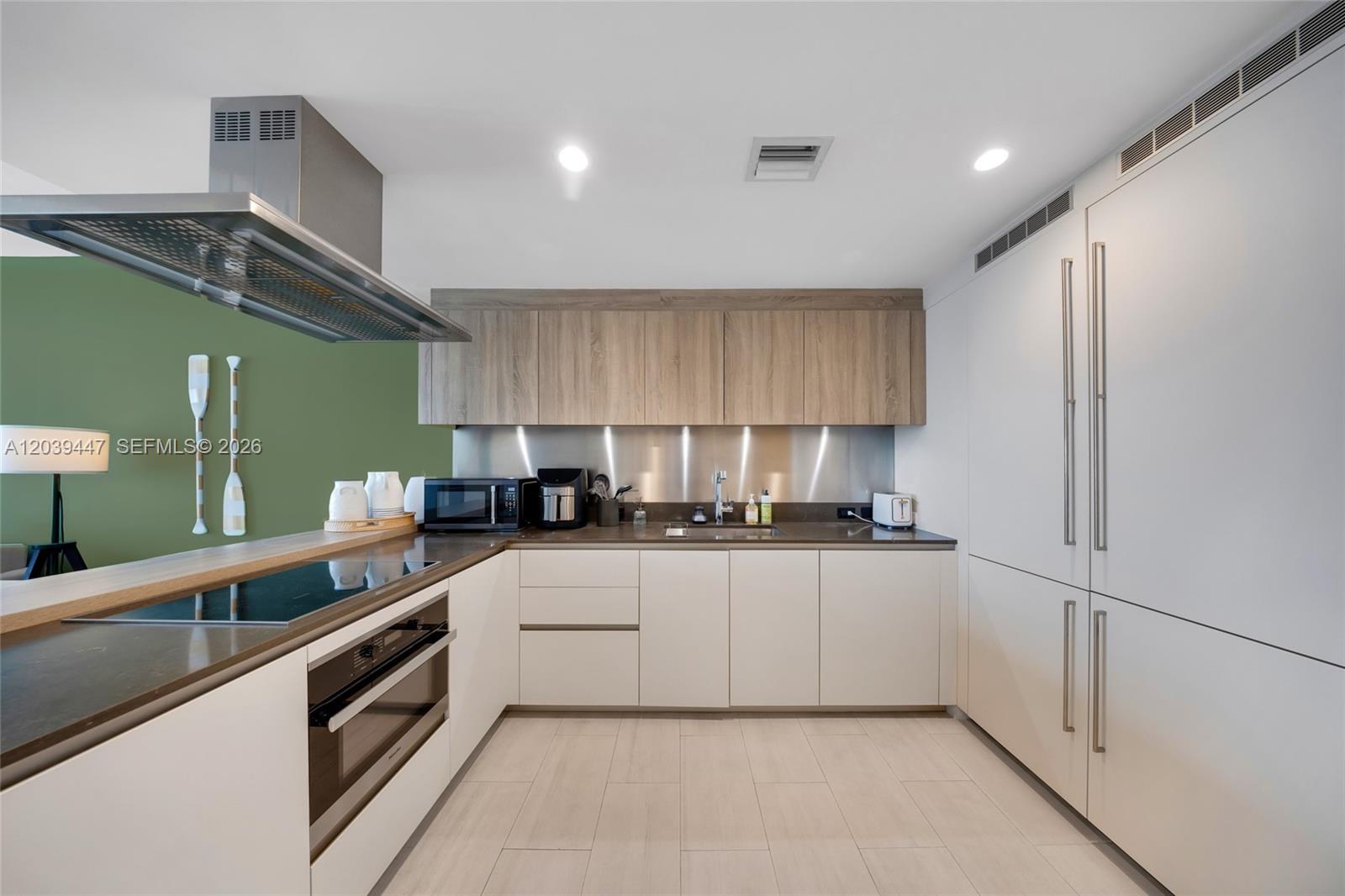 A modern kitchen features white cabinetry, wood-toned upper cabinets, a stainless steel backsplash, and appliances — 1000 Brickell Plz # 4704, Miami FL 33131, MIAMI, FL