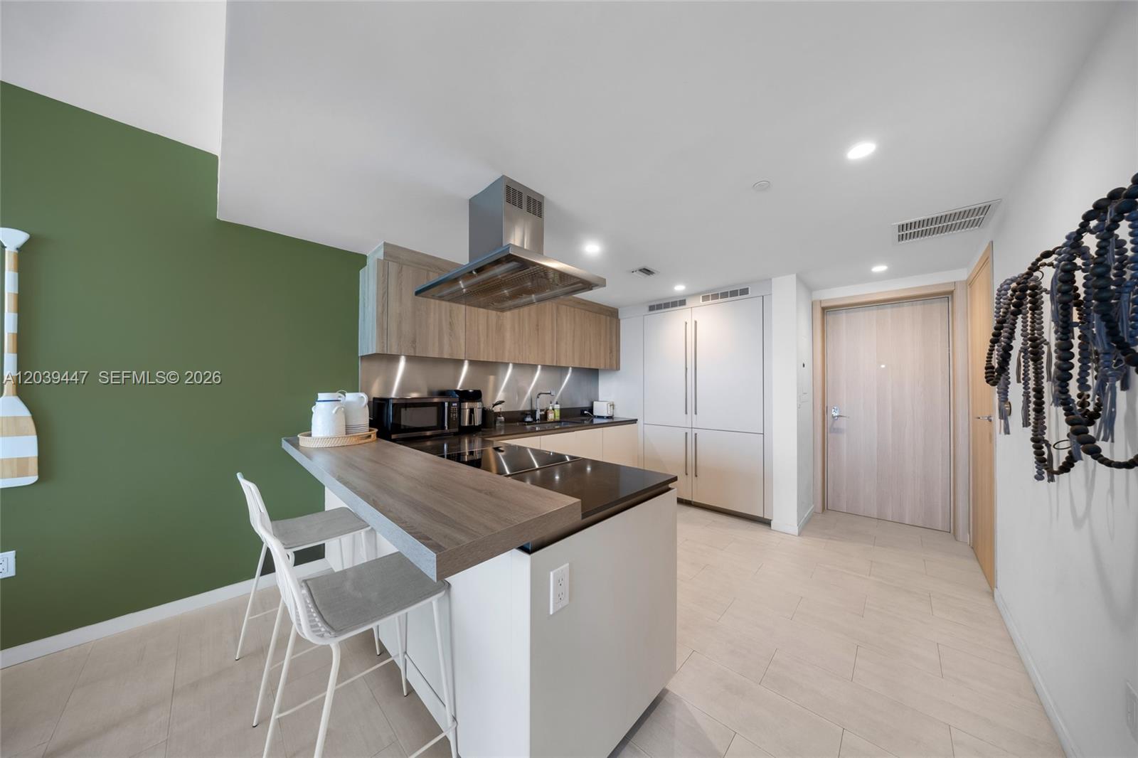 A modern kitchen features a breakfast bar, stainless steel range hood, and green accent wall — 1000 Brickell Plz # 4704, Miami FL 33131, MIAMI, FL
