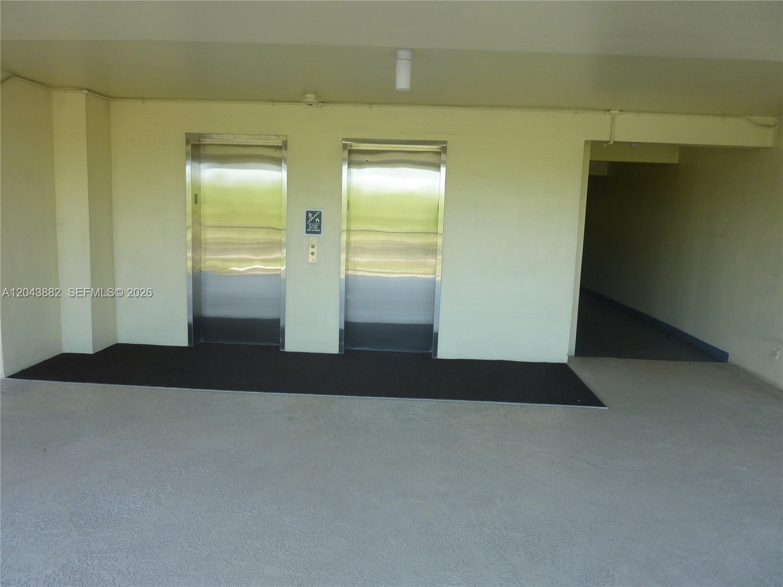 Two stainless steel elevators are set into a beige wall next to a dark hallway — 3200 N Palm Aire Dr # 305, Pompano Beach FL 33069, POMPANO BEACH, FL