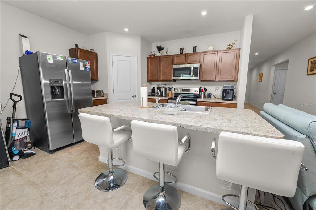 A kitchen features a granite-topped island with three white stools and stainless steel appliances — 913 EAGLE ROCK TERRACE, WINTER HAVEN, FL