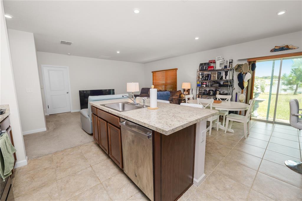 A kitchen island with a stainless steel sink and dishwasher sits before a dining area — 913 EAGLE ROCK TERRACE, WINTER HAVEN, FL