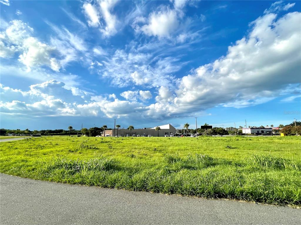 A large, grassy vacant lot sits under a bright blue sky with scattered clouds — 729 N 14TH ST / US HWY 27, LEESBURG, FL