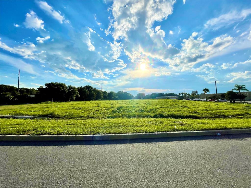 A large, grassy vacant lot is viewed from an adjacent paved road under a sunny sky — 729 N 14TH ST / US HWY 27, LEESBURG, FL