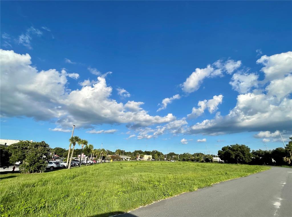 A large, grassy vacant lot sits under a bright blue sky with scattered clouds — 729 N 14TH ST / US HWY 27, LEESBURG, FL