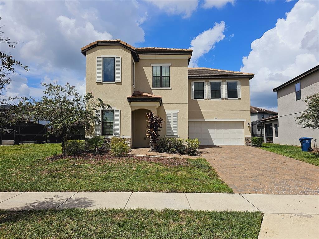 A two-story tan stucco house features a tiled roof, a paved driveway, and a garage — 191 AIDANS LANDING, HAINES CITY, FL