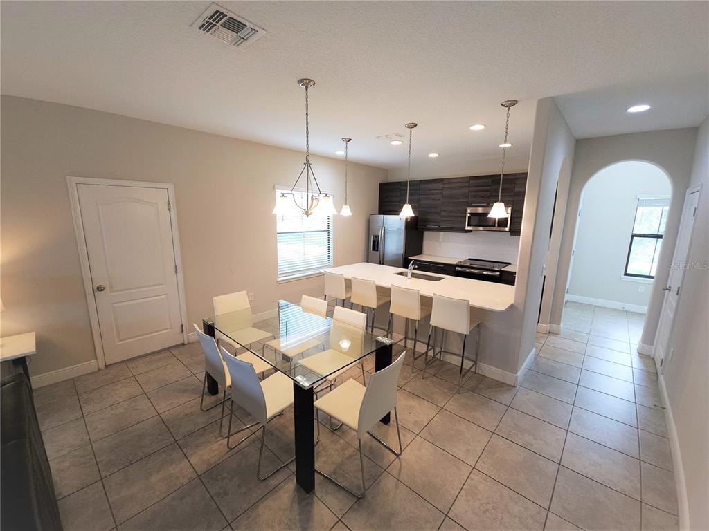 A dining area with a glass table and chairs sits adjacent to a modern kitchen island — 191 AIDANS LANDING, HAINES CITY, FL
