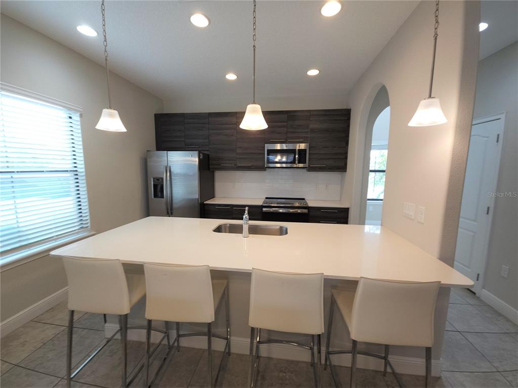 A kitchen features a large white island with bar seating, dark cabinets, and stainless appliances — 191 AIDANS LANDING, HAINES CITY, FL