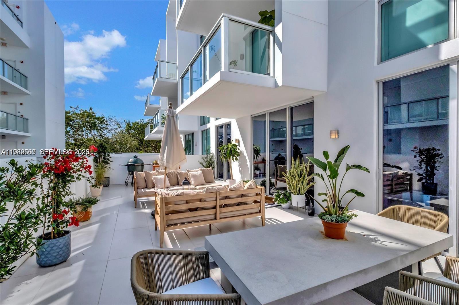 A spacious outdoor patio features modern furniture, potted plants, and a grill under a clear sky — 720 NE 62nd St # 307, Miami FL 33138, MIAMI, FL