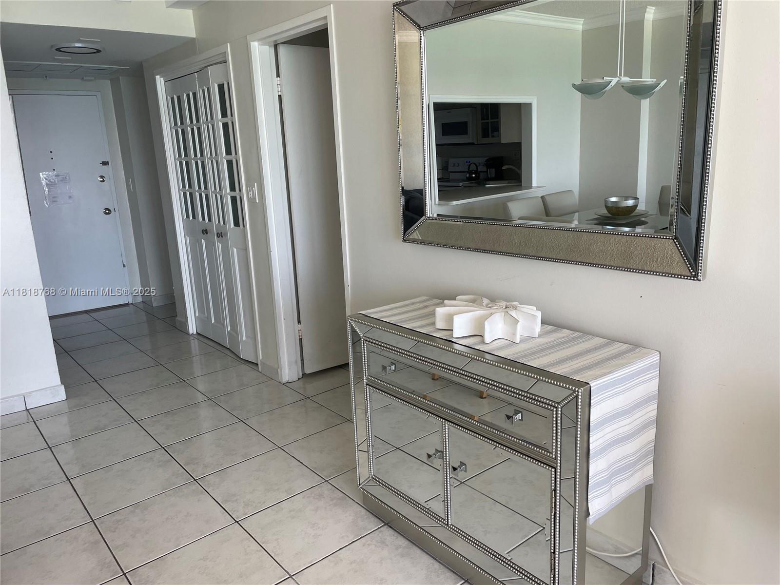A mirrored console table and wall mirror sit in a tiled hallway with white doors — 5601 Collins # 1210, Miami Beach FL 33140, MIAMI BEACH, FL