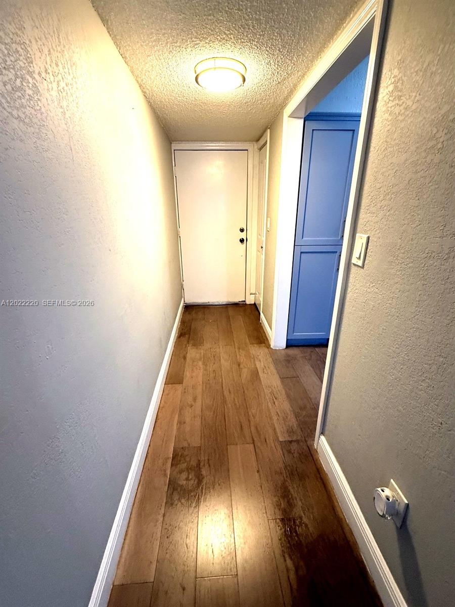 A hallway with wood-look flooring leads to a white door and a blue cabinet — 1635 W 44th Pl # 311, Hialeah FL 33012, HIALEAH, FL