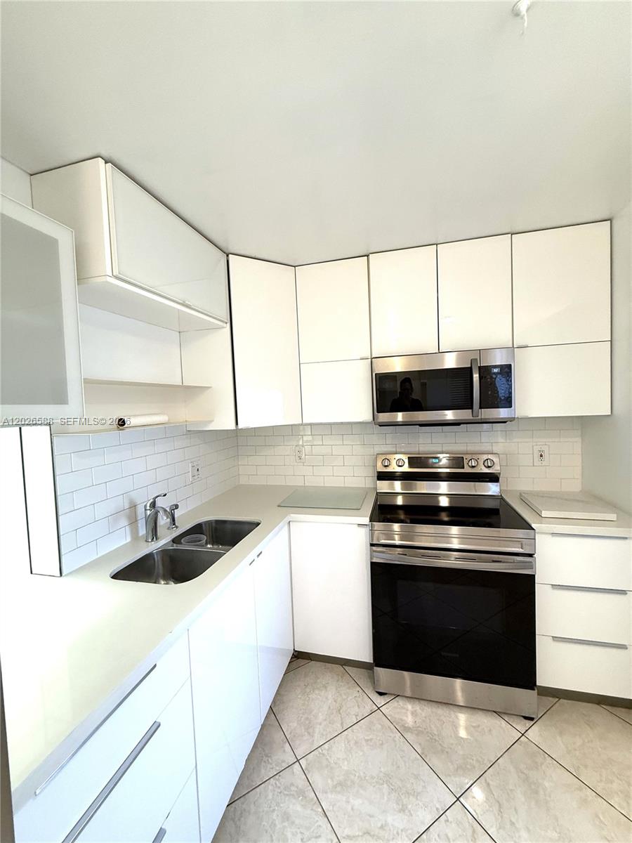 A modern kitchen features white cabinets, stainless steel appliances, and a white subway tile backsplash — 300 NE 14th Ave # 307, Hallandale Beach FL 33009, HALLANDALE BEACH, FL