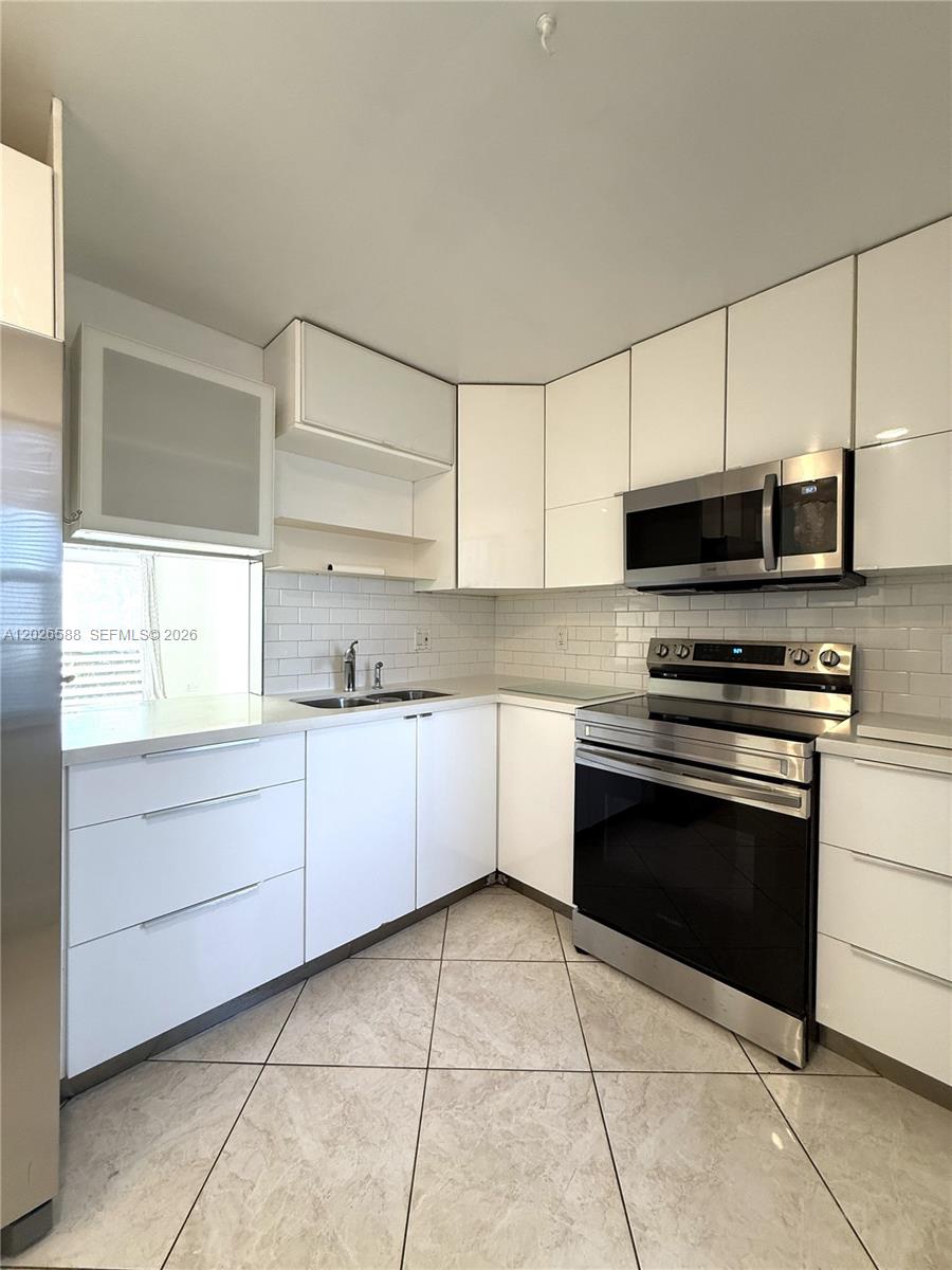 A modern kitchen features white cabinets, stainless steel appliances, and light-colored tile flooring — 300 NE 14th Ave # 307, Hallandale Beach FL 33009, HALLANDALE BEACH, FL