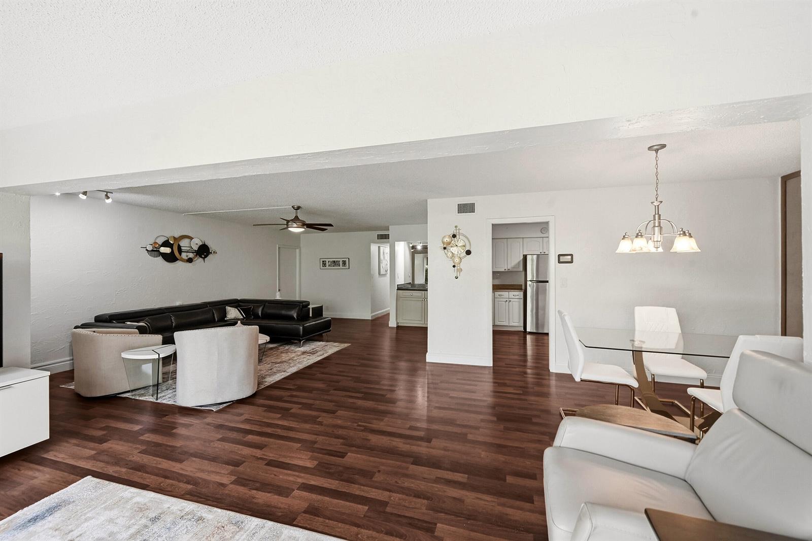 An open-concept living and dining area features dark wood floors, white walls, and modern furniture — 6612 Spring Bottom Way # 186, Boca Raton FL 33433, BOCA RATON, FL
