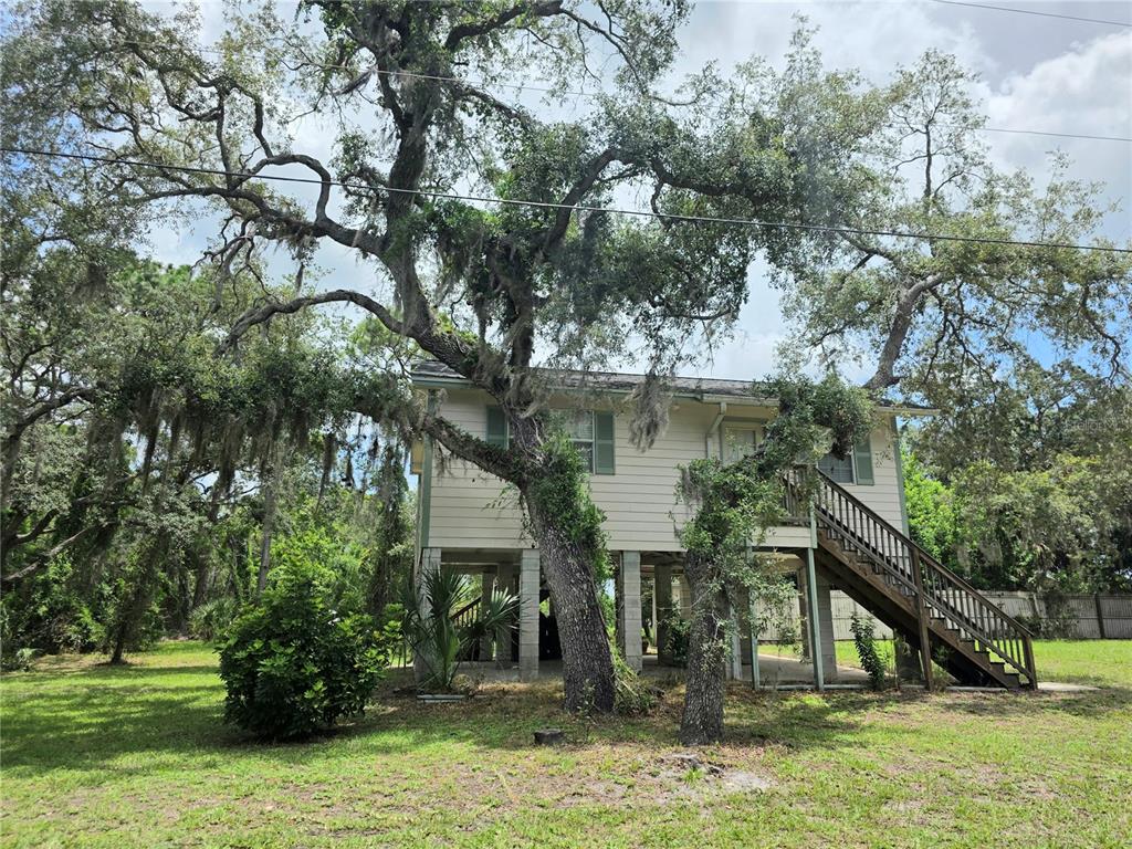A two-story house on stilts sits in a grassy yard surrounded by large oak trees — 14722 FAIR OAK WAY, HUDSON, FL
