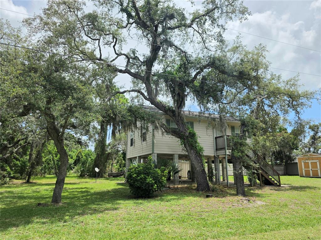 A two-story house on stilts sits in a grassy yard surrounded by large oak trees — 14722 FAIR OAK WAY, HUDSON, FL