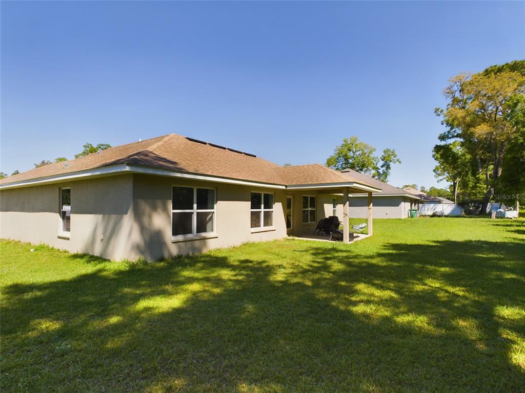 The rear exterior of a single-story house features a covered patio and a grassy yard — 3962 NE 58TH CIRCLE, SILVER SPRINGS, FL