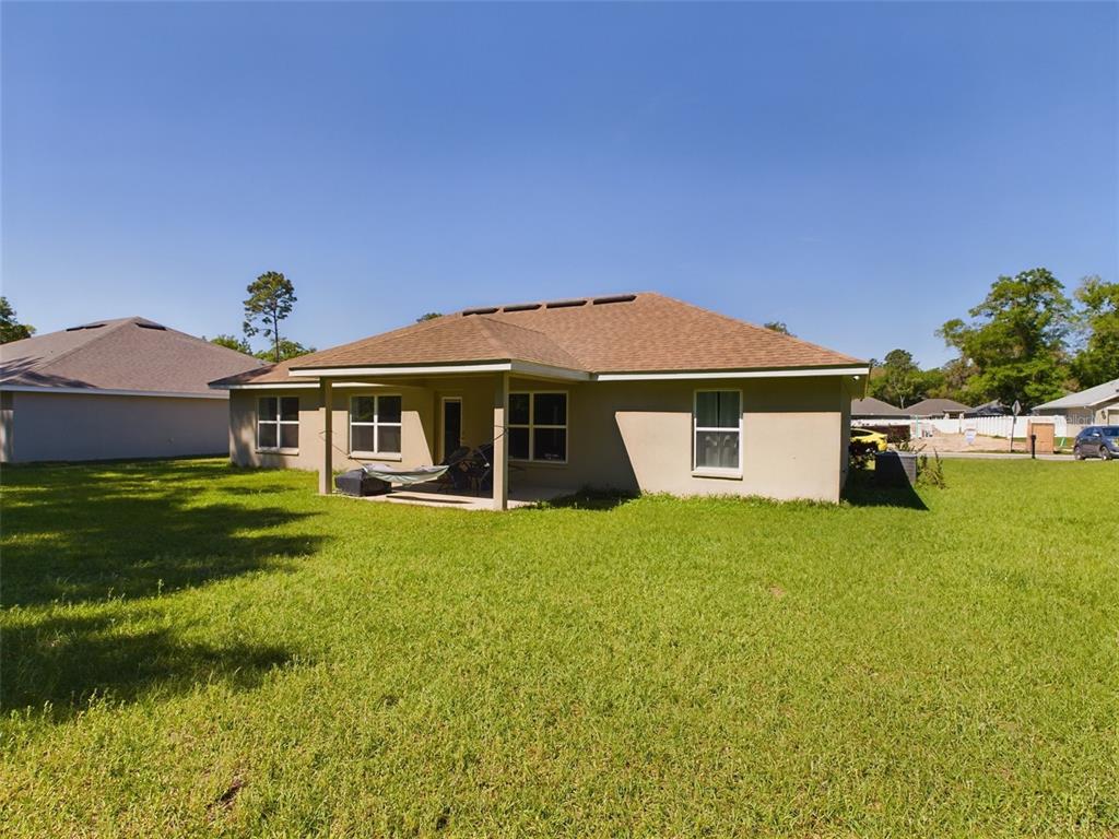 The rear exterior of a single-story house features a covered patio and a large lawn — 3962 NE 58TH CIRCLE, SILVER SPRINGS, FL