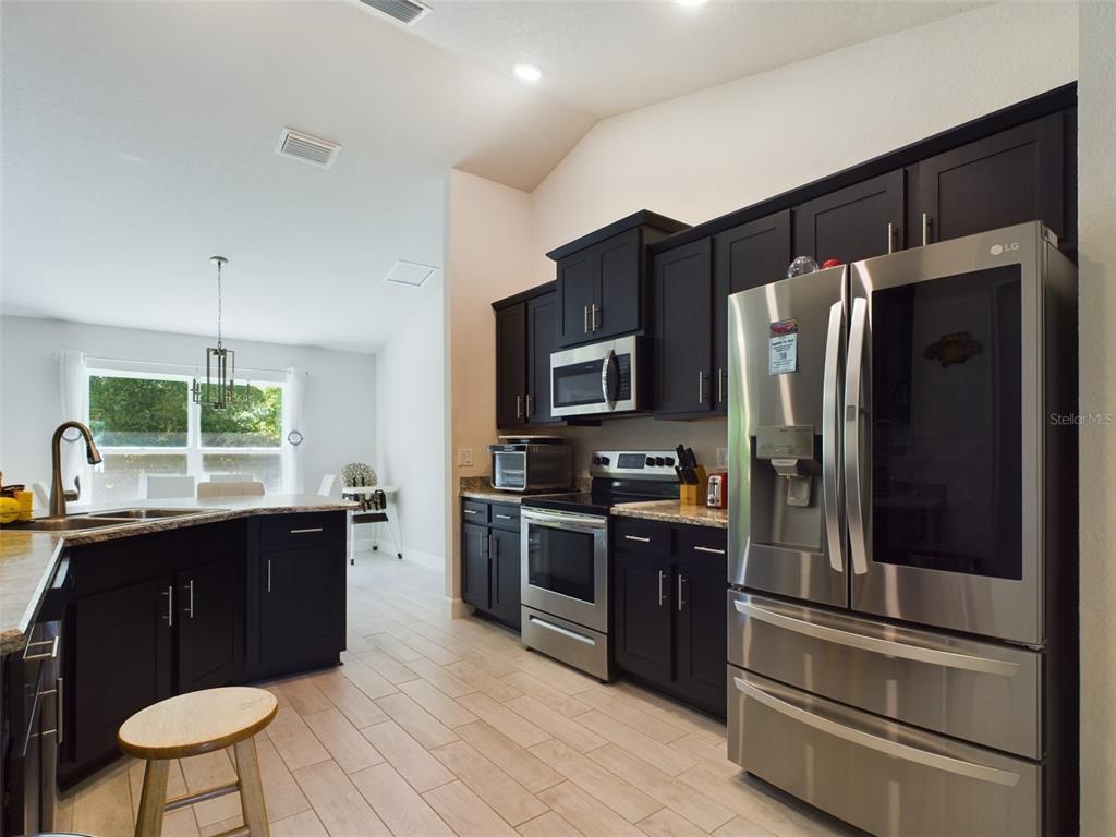 A kitchen features dark cabinets, stainless steel appliances, granite countertops, and light-colored tile flooring — 3962 NE 58TH CIRCLE, SILVER SPRINGS, FL