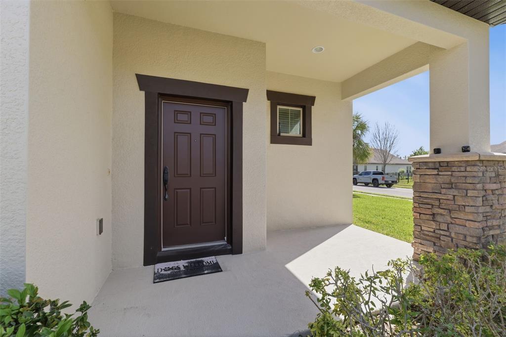 A covered front porch features a dark brown door, a small window, and stone accents — 4924 BUTLER NATIONAL DRIVE, WESLEY CHAPEL, FL