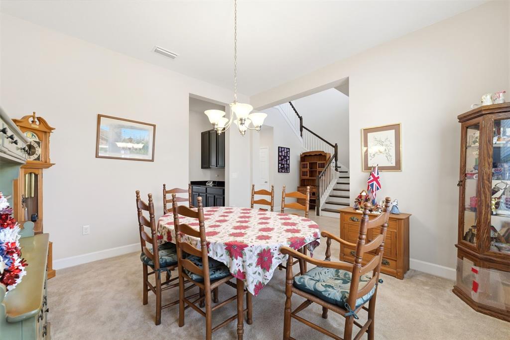 A dining room features a round table with a floral tablecloth, wooden chairs, and carpet — 4924 BUTLER NATIONAL DRIVE, WESLEY CHAPEL, FL