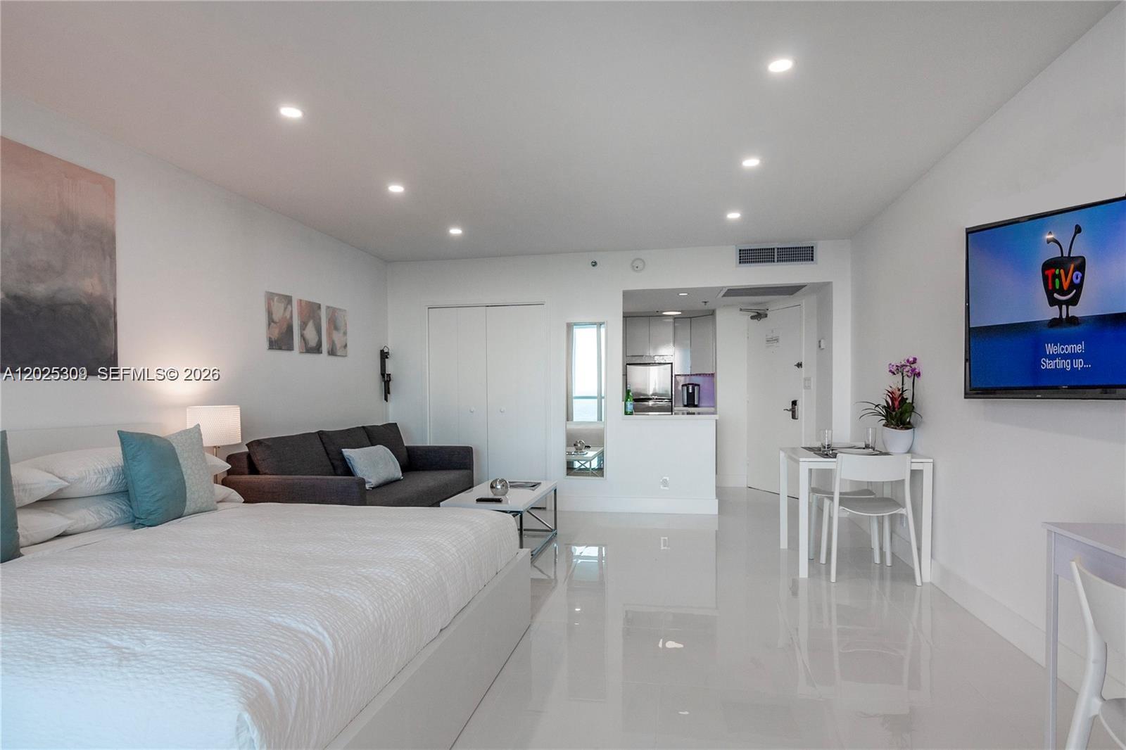 A studio apartment features a bed, sofa, dining table, and kitchen area with white floors — 5445 Collins Ave # 928, Miami Beach FL 33140, MIAMI BEACH, FL