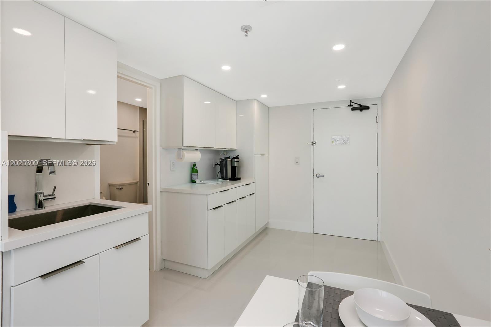 A minimalist white kitchen features flat-panel cabinetry, a stainless steel sink, and tile flooring — 5445 Collins Ave # 928, Miami Beach FL 33140, MIAMI BEACH, FL