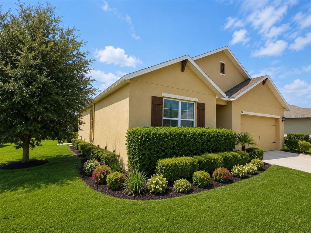A tan single-story house features a two-car garage, dark shutters, and manicured landscaping — 231 WILLOW BEND DRIVE, DAVENPORT, FL