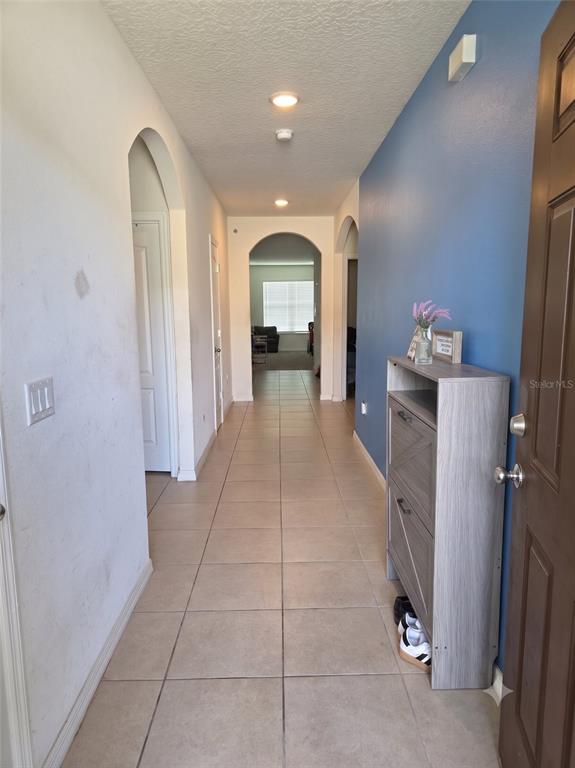 A hallway with tile flooring, a blue accent wall, and arched doorways leads to a room — 231 WILLOW BEND DRIVE, DAVENPORT, FL