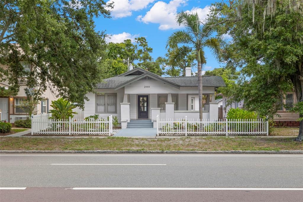 A white bungalow with a front porch and a picket fence sits behind a road — 2444 1ST AVENUE S, ST PETERSBURG, FL