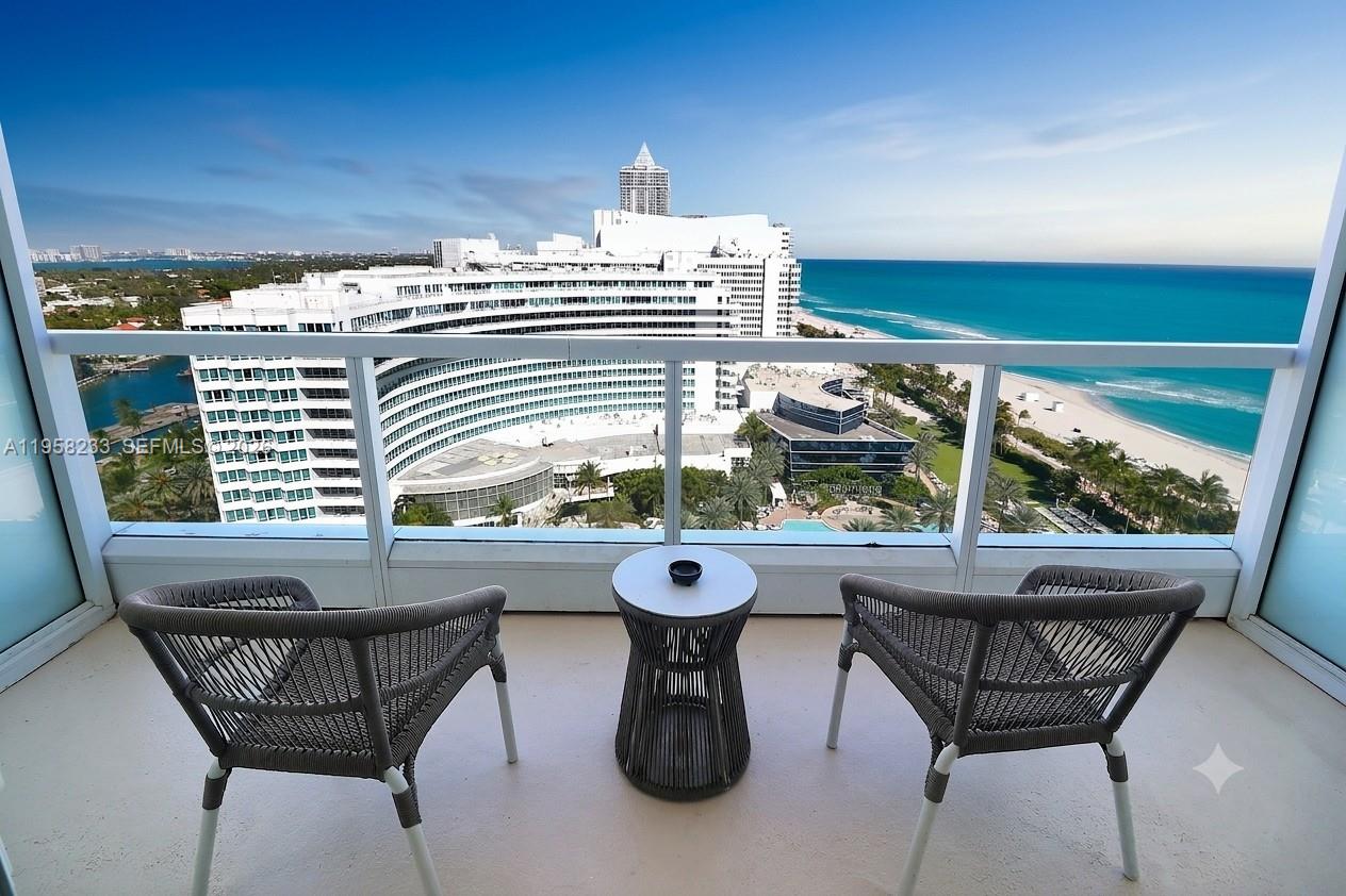 A balcony with two chairs and a small table overlooks a large hotel and beach — 4391 Collins Ave # 1703, Miami Beach FL 33140, MIAMI BEACH, FL