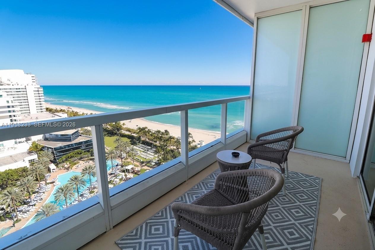 A balcony features two wicker chairs, a small table, and a patterned rug overlooking the ocean — 4391 Collins Ave # 1703, Miami Beach FL 33140, MIAMI BEACH, FL
