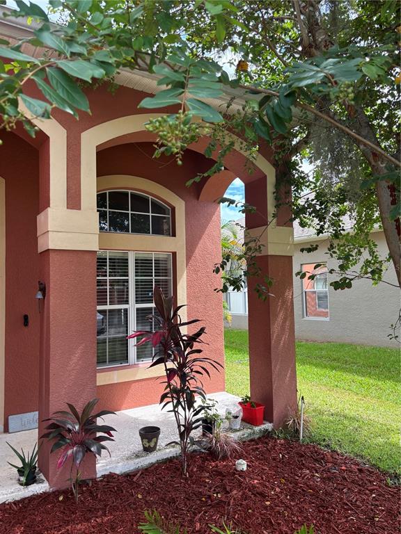 A red stucco house exterior features an arched entryway, a window, and a landscaped yard — 11153 SHELTER COVE LOOP, NEW PORT RICHEY, FL