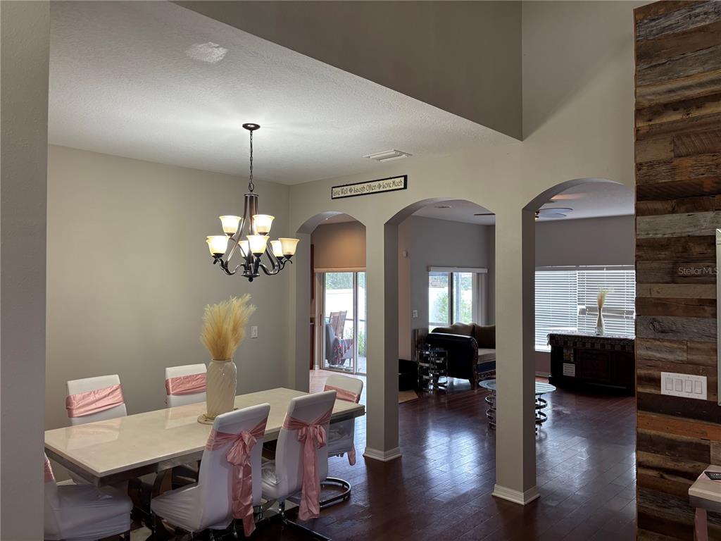 A dining room with a chandelier and table set leads into an adjacent living area — 11153 SHELTER COVE LOOP, NEW PORT RICHEY, FL
