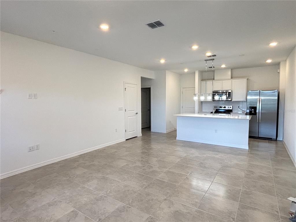 A kitchen with white cabinets and stainless steel appliances opens into a tiled living area — 11451 HARBORVIEW STREET, ORLANDO, FL