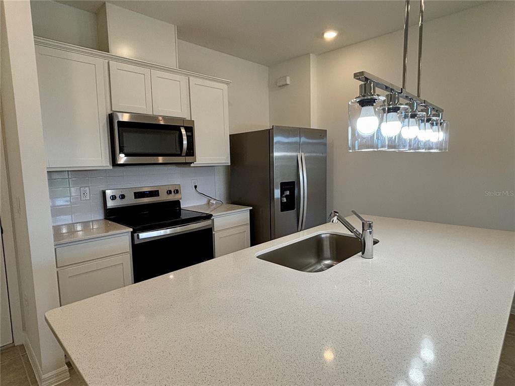 A kitchen features white cabinets, stainless steel appliances, a quartz island, and a pendant light — 11451 HARBORVIEW STREET, ORLANDO, FL