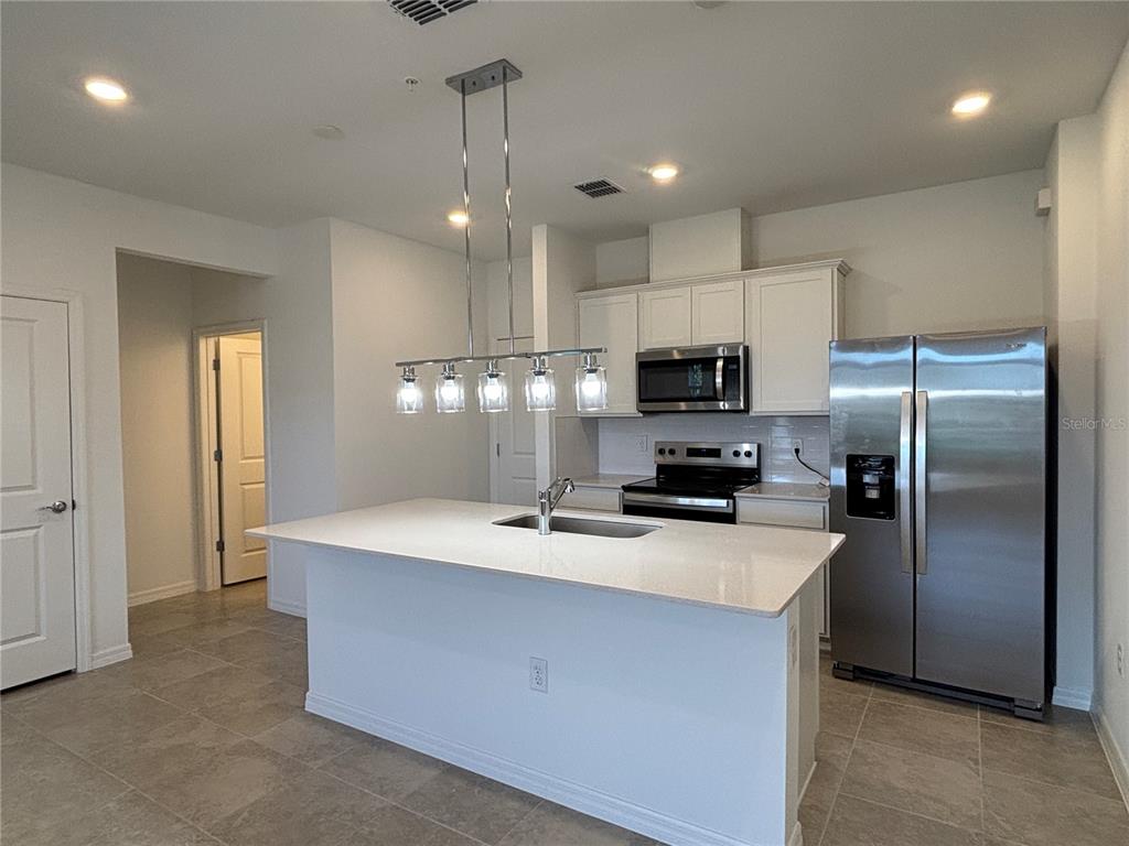 A kitchen features a white island with a sink, stainless steel appliances, and white cabinetry — 11451 HARBORVIEW STREET, ORLANDO, FL