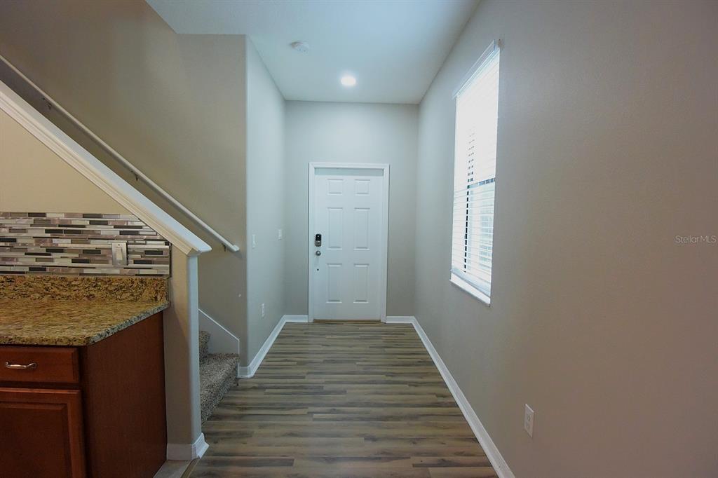 An entryway features wood-look flooring, a white front door, and stairs with a tiled backsplash — 20028 SATIN LEAF AVENUE, TAMPA, FL