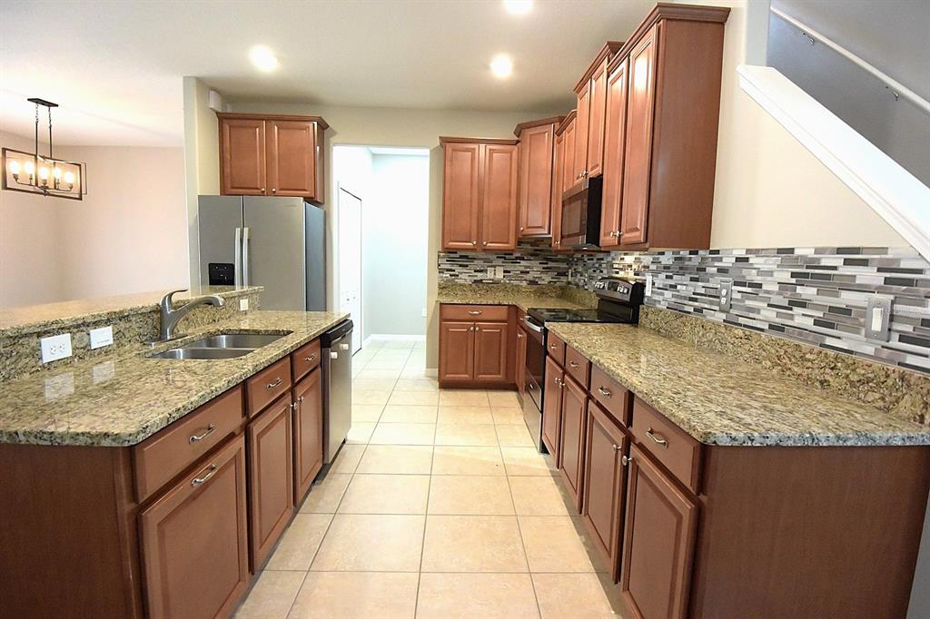 A kitchen features wood cabinets, granite countertops, a tile backsplash, and stainless steel appliances — 20028 SATIN LEAF AVENUE, TAMPA, FL
