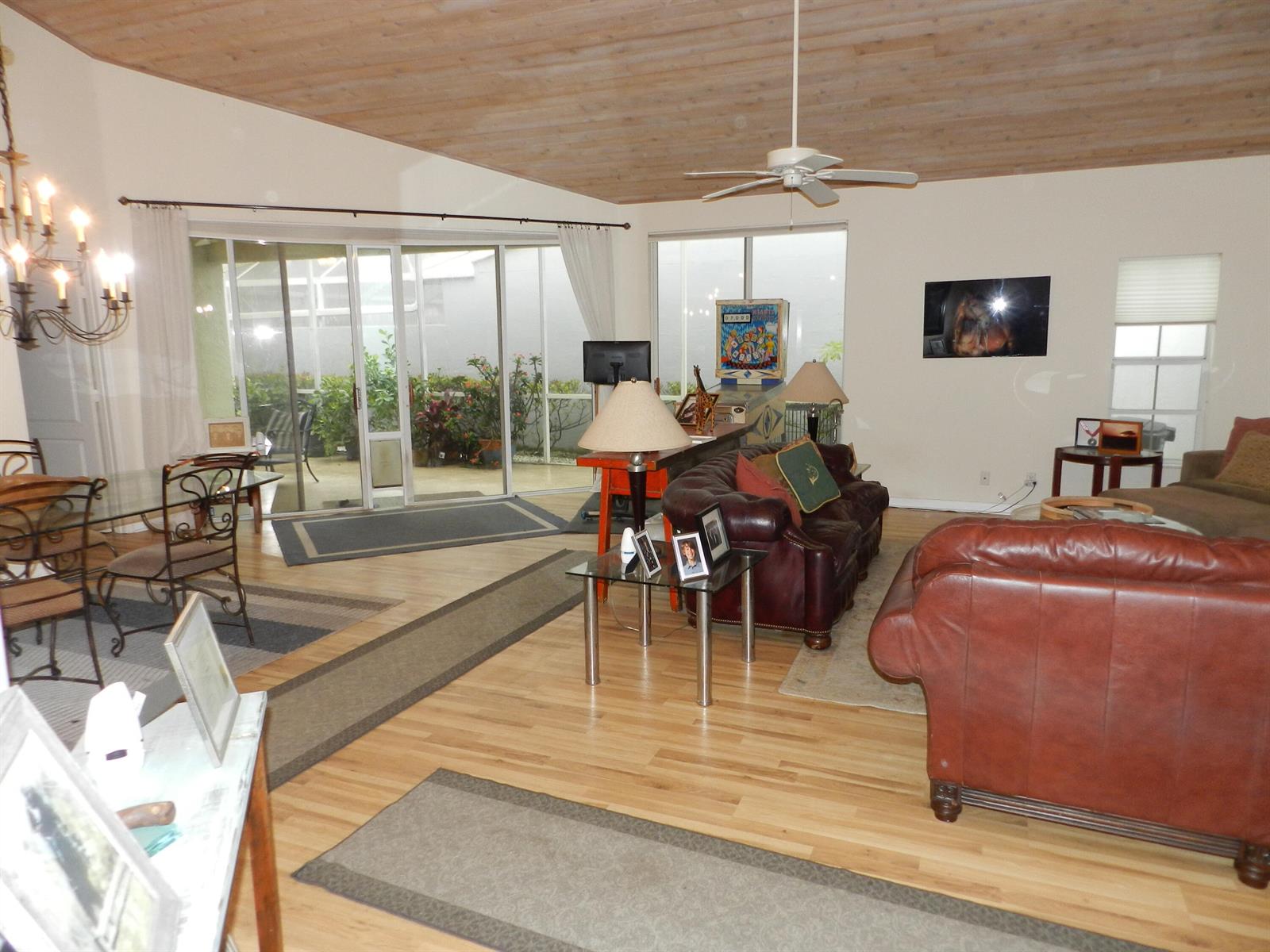 A living room with wood-plank ceilings, leather sofas, and sliding glass doors leading to a patio — 9198 Heathridge Drive, West Palm Beach FL 33411, WEST PALM BEACH, FL