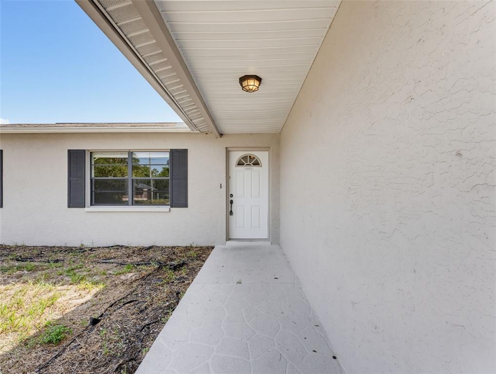 A white front door with a small arched window sits under a covered entryway — 4526 BAYRIDGE COURT, SPRING HILL, FL