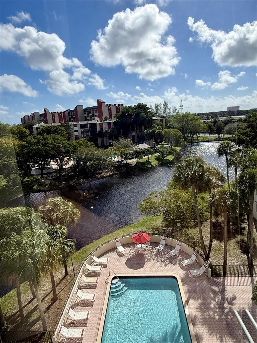 An elevated view of a swimming pool, patio, and pond surrounded by trees and buildings — 2304 S Cypress Bend Drive # 615, Pompano Beach FL 33069, POMPANO BEACH, FL