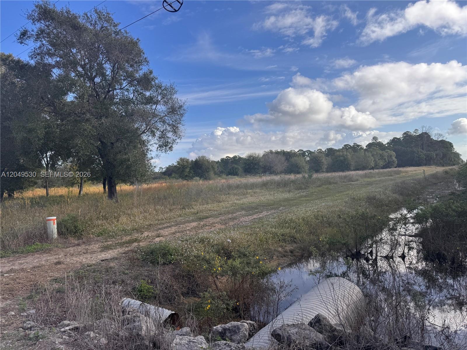 A dirt path leads through a grassy field past a drainage ditch and culvert — 775 S Hacienda St, Clewiston FL 33440, CLEWISTON, FL