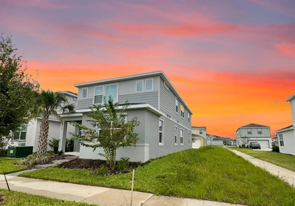 A two-story gray house with a side yard under a vibrant sunset sky — 6475 BREEZE FILLED LANE, WINTER GARDEN, FL