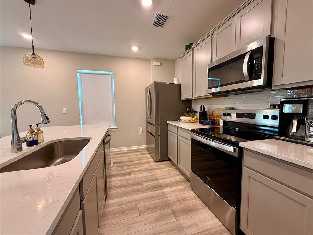 A modern kitchen features light gray cabinets, stainless steel appliances, and a white quartz island — 6475 BREEZE FILLED LANE, WINTER GARDEN, FL