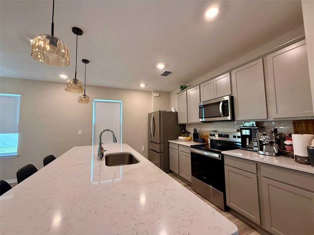 A kitchen features a large quartz island, gray cabinets, stainless steel appliances, and pendant lighting — 6475 BREEZE FILLED LANE, WINTER GARDEN, FL